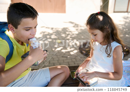 Children enjoying a snack outdoors on a sunny day Children enjoying a snack outdoors on a sunny day 118845749