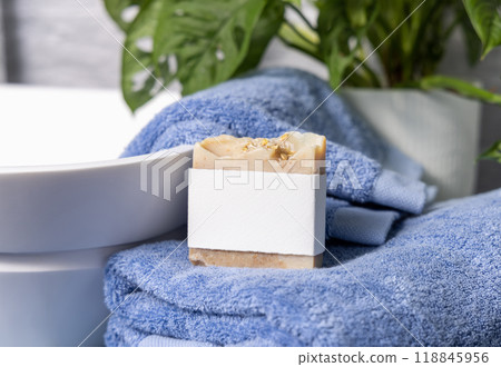 Soap bar with blank label on blue towels near vessel sink and green plant close up, mockup 118845956