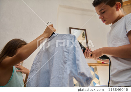 Young siblings ironing clothes together in a bright room 118846046