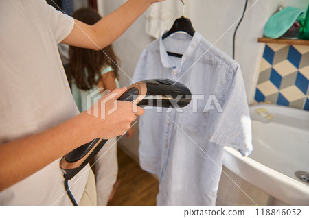 Man using a handheld steamer on a shirt indoors Man using a handheld steamer on a shirt indoors 118846052