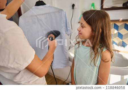 Young girl observes shirt being steamed at home 118846058