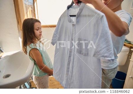 Young siblings handling laundry in a bright bathroom setting 118846062