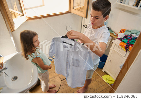 Brother helping sister choose outfit in sunny laundry room 118846063