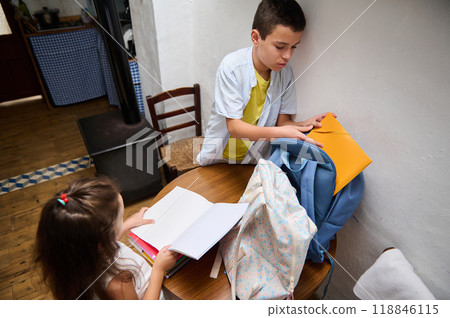 Children organizing school supplies into colorful backpacks in a cozy home setting Children organizing school supplies into colorful backpacks in a cozy home setting 118846115
