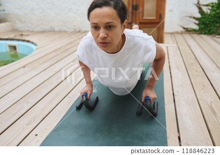 Woman engaging in outdoor push-up exercise with push-up bars on a wooden deck, focusing on upper body strength and fitness. 118846223
