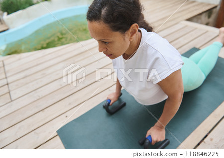 Woman practicing yoga on a mat outdoors, performing a cobra pose for relaxation and strength, focused on her exercise routine Woman practicing yoga on a mat outdoors, performing a cobra pose for relaxation and strength, focused on her exercise routine 118846225