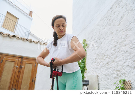 Woman exercising outdoors with resistance bands in a sunny courtyard setting 118846251
