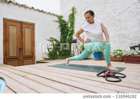 Woman practicing yoga on a wooden deck in an outdoor setting with plants and a serene atmosphere 118846282