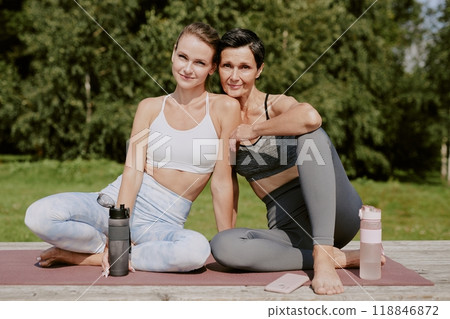 Portrait of beautiful mother and her beloved daughter sitting on yoga mat after train and posing for photo together 118846872