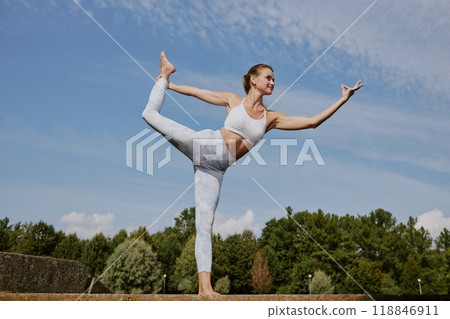 Low angle shot of young Caucasian woman dressed in fashionable and comfy sportswear practicing dancer pose in park 118846911