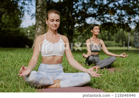 Young mom and her senior mom mediating in green park, they sitting on yoga mats and immersed in thoughts 118846946