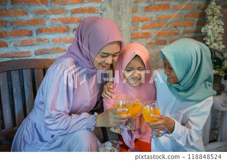 Asian Muslim mother and her two daughters joke over a drink celebrating Eid 118848524