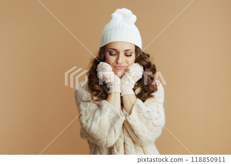sad elegant woman in beige sweater, mittens and hat on beige 118850911