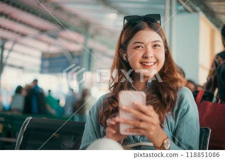 A young woman is smiling as she easily uses her smartphone in a busy airport A young woman is smiling as she easily uses her smartphone in a busy airport 118851086