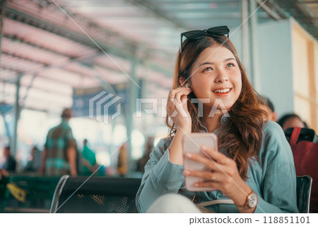 A Smiling Young Woman Using Her Smartphone in a Modern Airport Lounge Environment A Smiling Young Woman Using Her Smartphone in a Modern Airport Lounge Environment 118851101