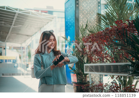 A Young Woman is Checking the Time on Her Phone in a Vibrant Outdoor Environment A Young Woman is Checking the Time on Her Phone in a Vibrant Outdoor Environment 118851139