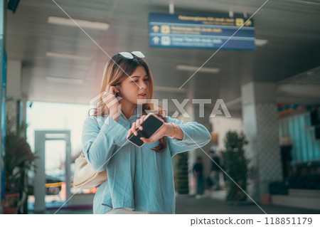 A young woman is checking the time on her smartphone at the airport gate 118851179