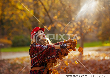 happy trendy woman in red hat throwing autumn leafs 118851520