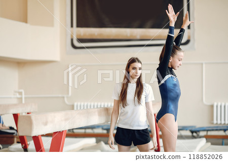 Child gymnastics balance beam. Girl gymnast athlete during an exercise horizontal bar in gymnastics competitions. Coach with child. Child gymnastics balance beam. Girl gymnast athlete during an exercise horizontal bar in gymnastics competitions. Coach with child. 118852026