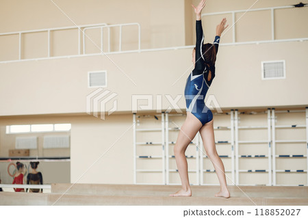 Child gymnastics balance beam. Girl gymnast athlete during an exercise horizontal bar in gymnastics competitions. 118852027