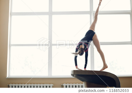 Child gymnastics balance beam. Girl gymnast athlete during an exercise horizontal bar in gymnastics competitions. Child gymnastics balance beam. Girl gymnast athlete during an exercise horizontal bar in gymnastics competitions. 118852033