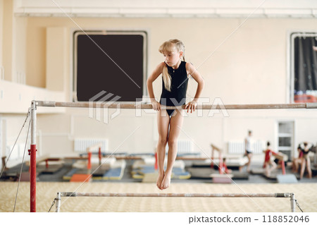 Child gymnastics balance beam. Girl gymnast athlete during an exercise horizontal bar in gymnastics competitions. Child gymnastics balance beam. Girl gymnast athlete during an exercise horizontal bar in gymnastics competitions. 118852046
