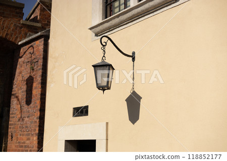 Old antique metal lamp at the old wall. Victorian vintage street lantern at the day time, turned off. The wall lamp on the old street 118852177