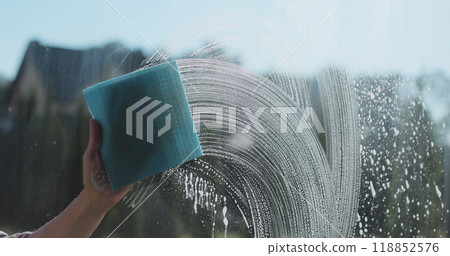 Woman in rubber gloves sprays window cleaner from a spray bottle onto the windows glass. Housewife hands in rubber gloves cleaning windows close up. Cleaning glass window with a cloth special rag blue 118852576