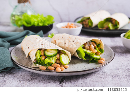 Tortilla wraps with cucumber, white beans and lettuce on a plate on a table 118853323