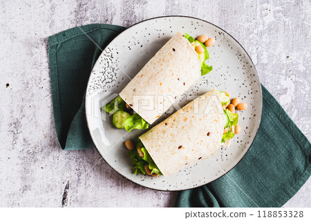 Close up of tortilla wraps with cucumber, white beans and lettuce on a plate on a table top view Close up of tortilla wraps with cucumber, white beans and lettuce on a plate on a table top view 118853328