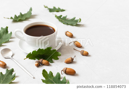 Coffee in a white cup with oak leaves and acorns on white background closeup. Autumn cozy still life with black coffee. Copy space. Coffee in a white cup with oak leaves and acorns on white background closeup. Autumn cozy still life with black coffee. Copy space. 118854073