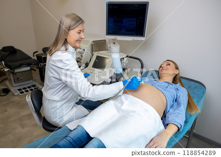 Long-haired mature doctor doing ultrasonography to a pregnant woman 118854289