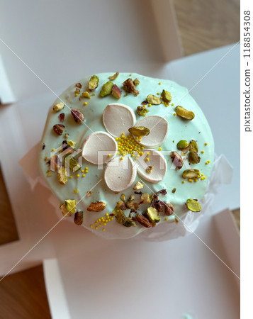 Beautifully decorated cake on a table, adorned with green icing and sprinkled with nuts and meringue pieces. Pastry is wrapped elegantly, perfect treat for special holidays. Sweet food and delicious Beautifully decorated cake on a table, adorned with green icing and sprinkled with nuts and meringue pieces. Pastry is wrapped elegantly, perfect treat for special holidays. Sweet food and delicious 118854308