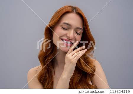 Cute young woman with long ginger hair on a grey background Cute young woman with long ginger hair on a grey background 118854319