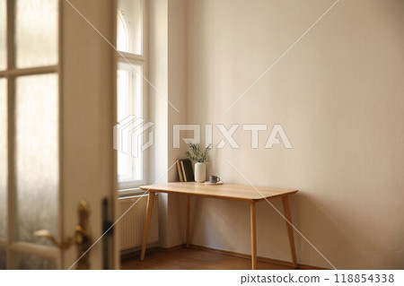 Living room view through blurred open white door. Vase with olive branches. Parquet floor. Home office table near window. Minimal Scandi boho interior. Cup of tea, coffee. Empty beige wall background. 118854338