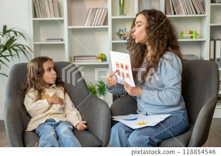 Long-haired cute girl working with a speech therapist and looking attentive 118854546