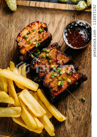 Close-up of barbecue ribs with crispy fries on a wooden board, served with a side of dipping sauce Close-up of barbecue ribs with crispy fries on a wooden board, served with a side of dipping sauce 118855192