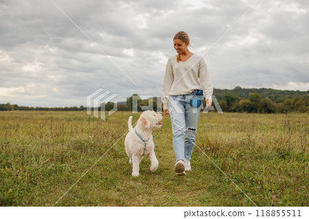 A woman is walking with her dog in a beautiful and scenic outdoor field on a lovely day 118855511