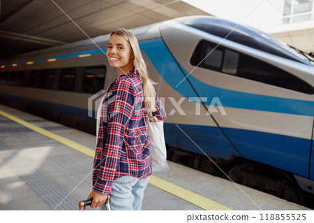 A Smiling Traveler Standing at a Train Station Next to a Modern Train, Ready for Adventure A Smiling Traveler Standing at a Train Station Next to a Modern Train, Ready for Adventure 118855525