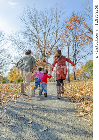 Back view of a family of four playing in a park with autumn leaves Back view of a family of four playing in a park with autumn leaves 118858259