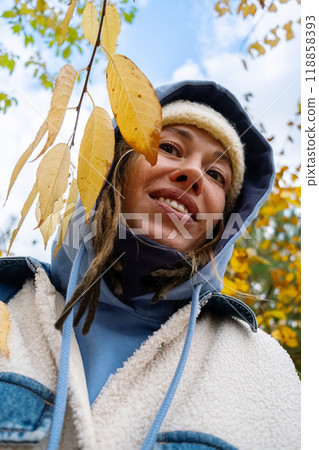Woman in autumn attire smiling under yellow leaves on sunny day. Enjoying fall outdoors concept. 118858393