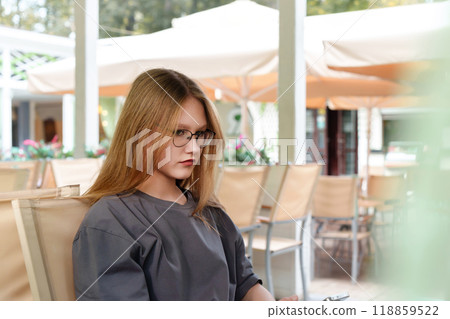 sullen-faced teenage appears offended as she sits alone in a cafe, conveying a sense of annoyance or displeasure 118859522