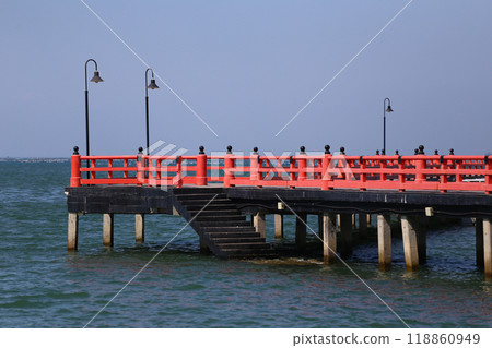Red bridge that extends into the sea and view of the blue sky background. 118860949