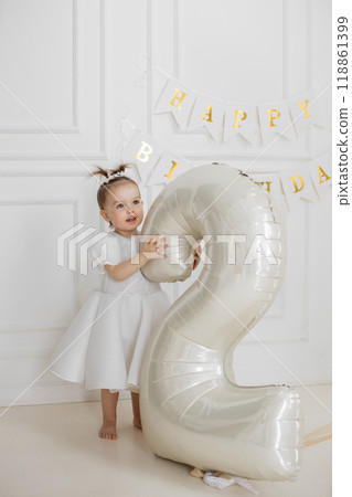 Little girl celebrating second birthday with big balloon indoors Little girl celebrating second birthday with big balloon indoors 118861399
