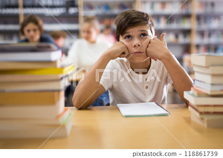 Bored teenage boy trying to prepare for exam in library 118861739