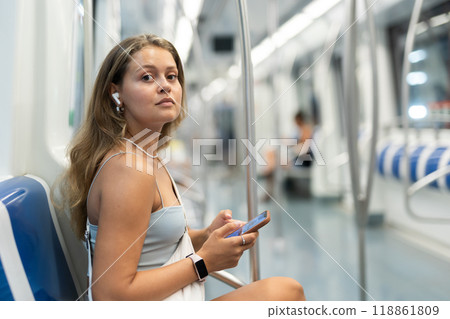 Woman sits in subway car with headphones and phone 118861809