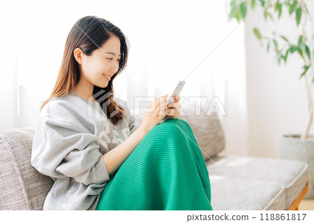 Woman sitting on a sofa and looking at a smartphone 118861817