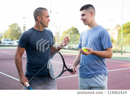Two men with rackets in their hands chatting after playing on tennis court 118862424