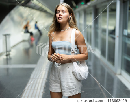 Girl with earphones is standing on subway platform, waiting for train to arrive 118862429