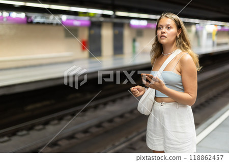 Young girl standing in platform with phone in hand 118862457